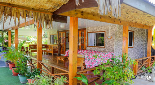 Villa tropicale à Moorea avec porche en bois, murs de briques, fleurs roses, plantes en pots et détails de toit en chaume
