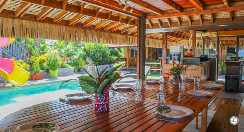 Zone de restauration de villa tropicale à Moorea avec terrasse en bois, table dressée, vue sur piscine et abri couvert de chaume