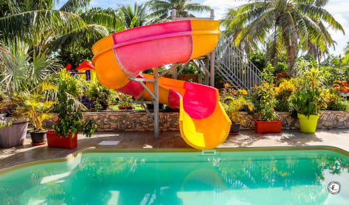 Toboggan aquatique en spirale colorée à côté d'une piscine turquoise à la villa Aimehome à Moorea avec jardins tropicaux