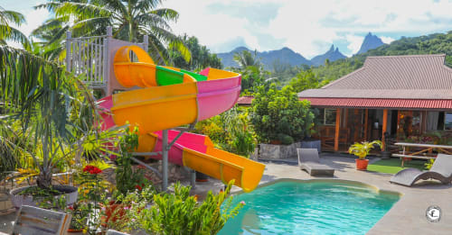 Toboggan aquatique coloré à la villa Aimehome à Moorea avec piscine turquoise, jardins tropicaux et vue sur les montagnes