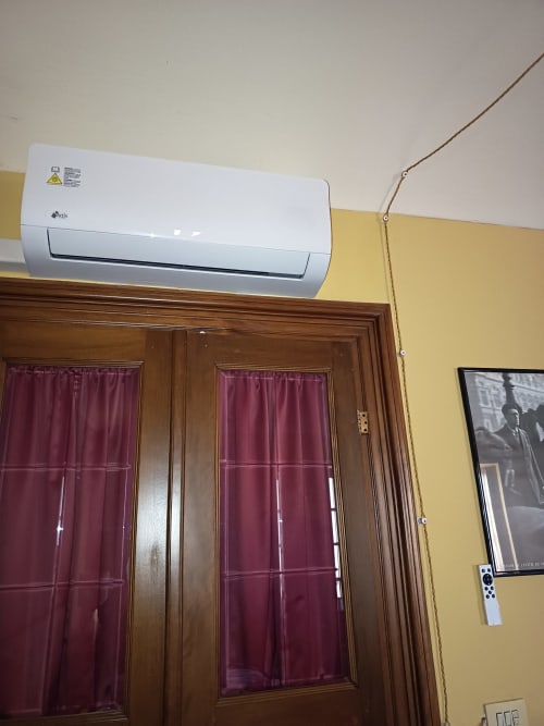 Unità di condizionamento aria split bianca montata sopra porte in legno con tende bordeaux nella stanza Puccini di Casa Armenia B&B