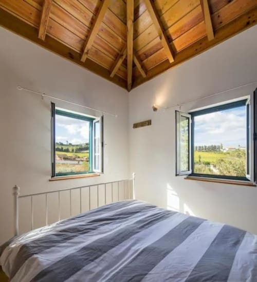 Bright bedroom with wooden ceiling, striped bedding, and countryside views at Quinta Boa Vida, Alcobaça