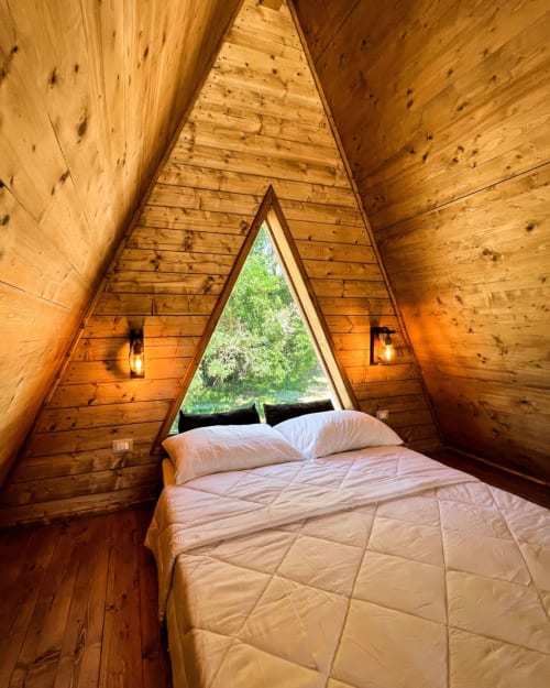 Accogliente camera A-frame in legno a Guarda Che Luna a Sasso di Castalda con letto, cuscini e finestra triangolare con vista