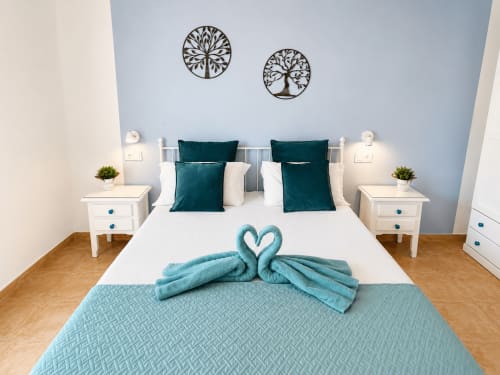 Dormitorio moderno en Apartamentos El Calón Playa con almohadas turquesas, mesitas blancas y arte mural de árbol decorativo