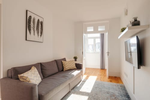 Sala de estar moderna no Bom Porto Apartments com sofá cinzento, TV, soalho em madeira e luz natural das portas envidraçadas