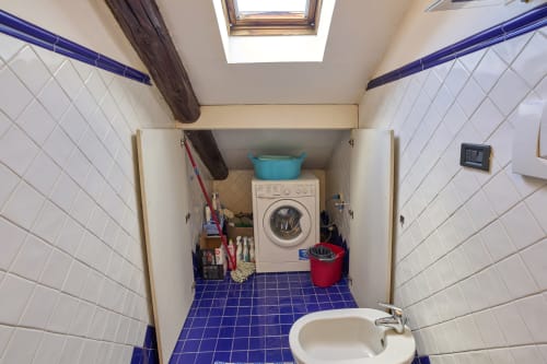 Lavanderia dell'appartamento B&B A Casa Armenia a Torino con lavatrice, lavandino, piastrelle bianche, pavimento blu e lucernario