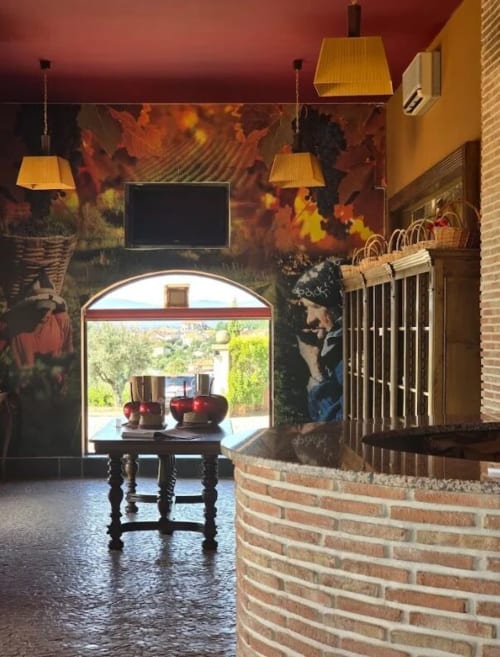 Entrada da adega Tranca da Barriga com arcada, lareira, luminárias pendentes e detalhes de tijolos rústicos em Covilhã