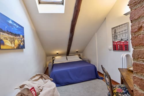 Accogliente camera da letto in soffitta presso A Casa Armenia B&B a Torino con coperta blu, mattoni a vista, lucernario e quadri con vista sulla città.