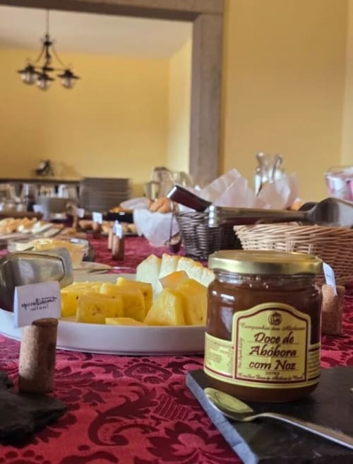 Mesa de café da manhã do hotel na Tranca da Barriga com conservas portuguesas, frutas frescas e cestos de vime em Covilhã