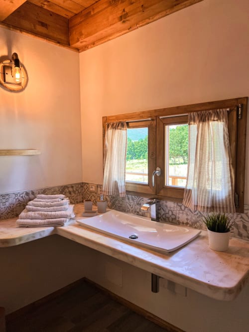Modern bathroom with double sink, mountain views through windows, wooden ceiling beams, towels, and terrace at Guarda Che
