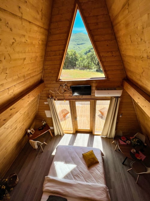 A-Frame glamping interior at Guarda Che Luna with bed, mountain view window, wooden walls, desk, and modern amenities in