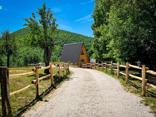 A-frame glamping cabin with metal roof nestled among green mountains and trees at Guarda Che Luna in Sasso di Castalda, Italy
