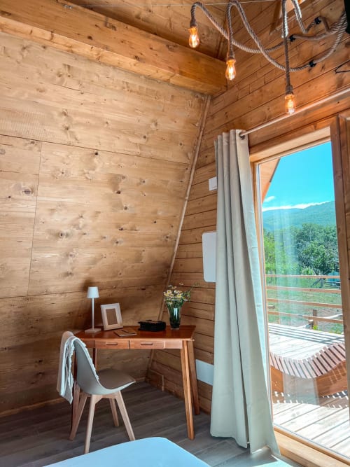 Modern A-frame glamping interior with wooden walls, desk, chair, and mountain view from terrace in Sasso di Castalda