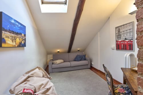 Accogliente monolocale in soffitta a Torino con divano grigio, lucernario, travi a vista e foto della città alle pareti