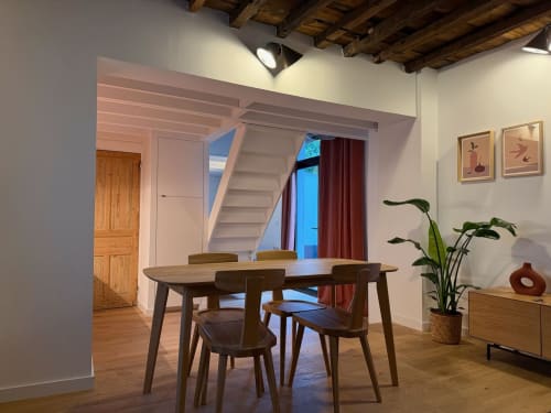 Salle à manger moderne de l'appartement Le 426 à Mouvaux, avec table en bois, chaises, escalier et vue sur le jardin à travers des rideaux rouges