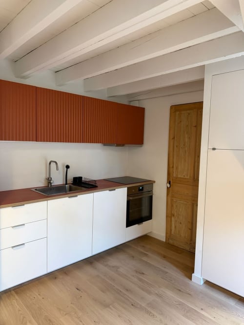 Kitchenette moderne avec armoires blanches, rangements rouges et porte en bois dans l'appartement Le426 à Mouvaux