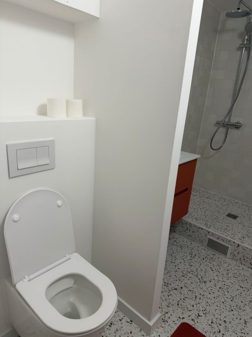 Salle de bain moderne du studio Le 426 à Mouvaux avec toilettes blanches, douche et sol à motifs