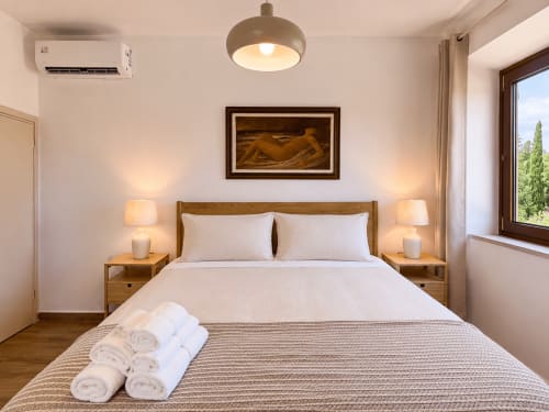 Elegant bedroom at Tuscan Sun Stays in Volterra with wooden bed, white linens, rolled towels, bedside lamps, and framed