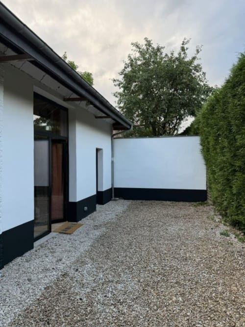 Façade moderne blanche du Le 426 à Mouvaux avec finitions noires, cour en gravier et haies vertes
