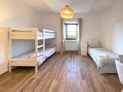 Bright multi-bed room at Tuscan Sun Stays in Volterra with wooden floors, bunk bed, single bed, and window with countryside