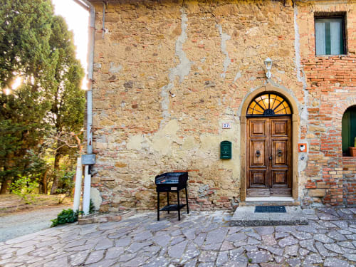 Historic stone building entrance in Volterra with wooden door, ivy, and black chair at Tuscan Sun Stays hotel