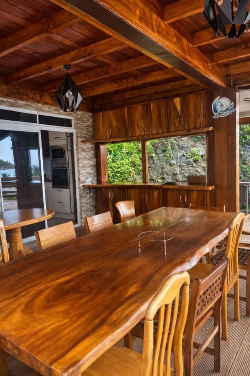 Salle à manger avec table et chaises en bois, poutres apparentes, vue sur l'océan par les fenêtres à Villa Vaipipiha, Paopao