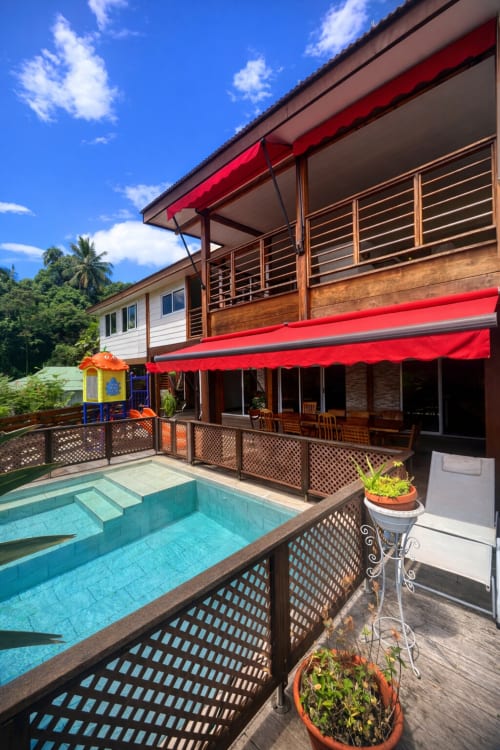 Piscine de la Villa Vaipipiha avec auvents rouges, balustrades en bois et végétation tropicale luxuriante à Paopao