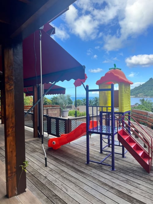 Aire de jeux colorée avec toboggan et tour sur terrasse en bois surplombant la baie tropicale à la villa Aimehome à Paopao