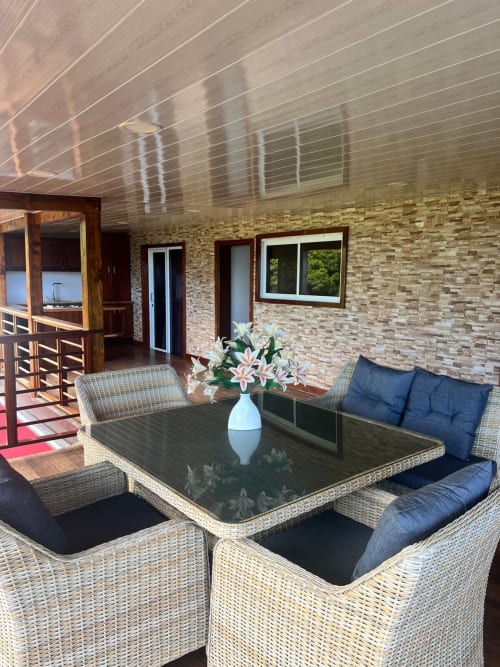 Terrasse couverte de la Villa Vaipipiha avec salon en rotin, table en verre et fleurs blanches à Paopao