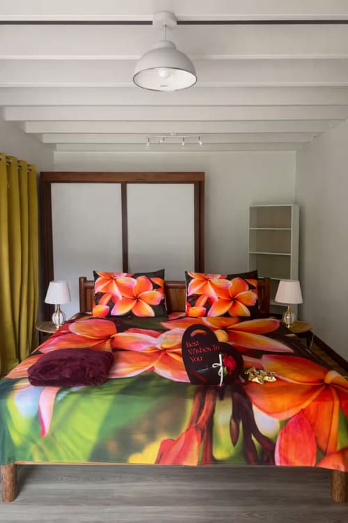 Chambre vibrante à Villa Vaipipiha avec parure fleurie colorée, lit à cadre en bois, luminaire blanc au plafond et rideaux jaunes