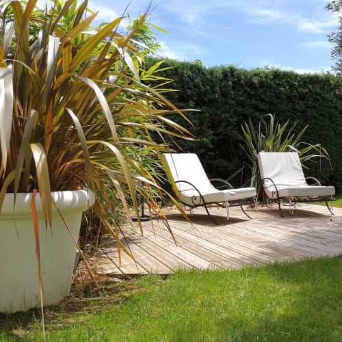 Jardine ensoleillée de La Bastide Des Muriers avec chaises longues sur terrasse bois, plantes tropicales et haies à Deaux, France