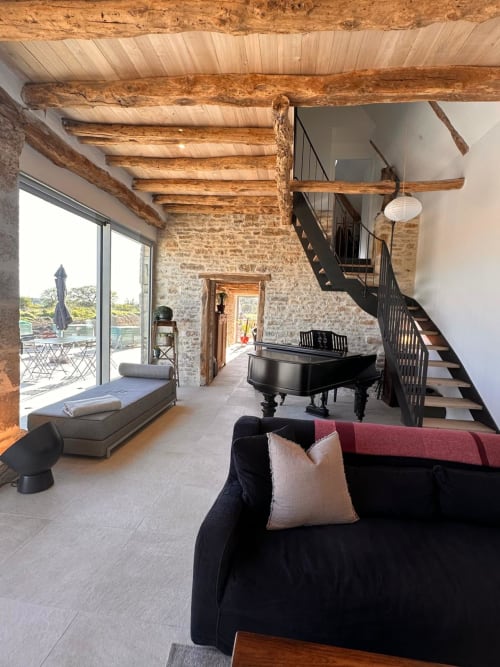 Spacieux loft de la Maison Lapopie avec poutres apparentes, grand piano, canapé noir et vue sur la terrasse à Saint-Cirq-Lapopie.