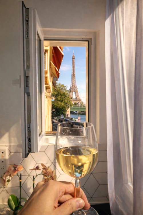 Main tenant un verre de vin blanc avec vue sur la Tour Eiffel depuis le balcon d'un appartement parisien