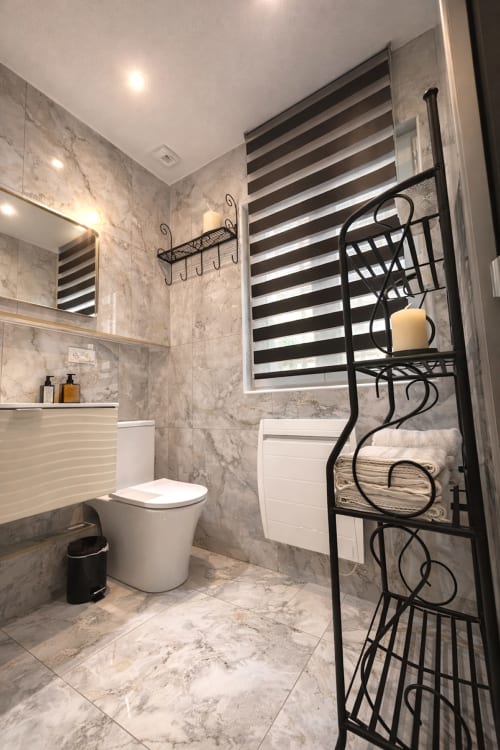 Salle de bain moderne d'un appartement parisien avec carrelage en marbre, toilettes blanches, lavabo, miroir et porte-serviettes en métal noir