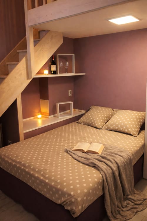 Chambre cosy d'appartement parisien avec parure à pois, escalier en bois, rangements intégrés et éclairage ambiant chaleureux