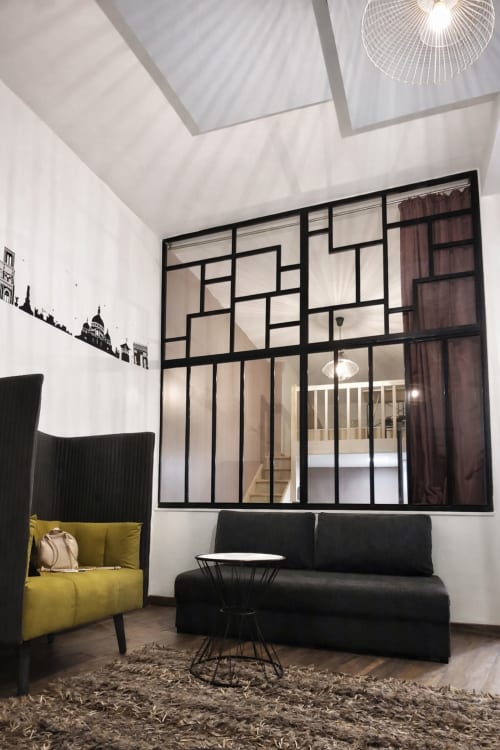 Salon moderne d'appartement parisien avec chaise jaune, canapé noir et fenêtre industrielle à l'hôtel ATHEA