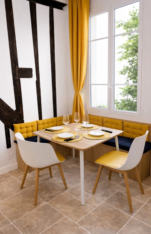 Salle à manger contemporaine à l'appartement ATHEA Paris avec banquette jaune, chaises blanches, table en bois et vue sur cour