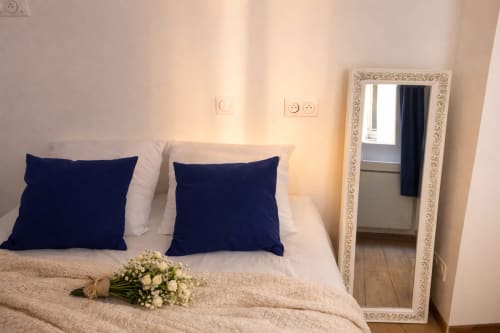 Chambre cosy d'appartement parisien avec lit blanc, coussins bleu marine, miroir décoratif et composition florale à ATHEA BnB