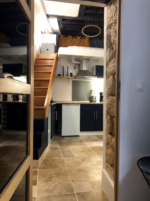 Cuisine d'appartement parisien moderne avec meubles noirs, électroménagers blancs, escalier en bois vers chambre mansardée, carrelage