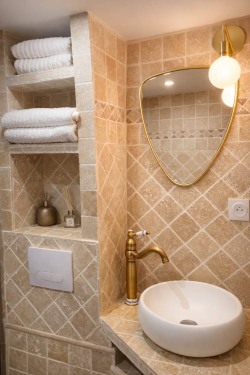 Salle de bain élégante de l'appartement ATHEA Paris avec miroir doré, carrelage marbre, vasque et serviettes blanches