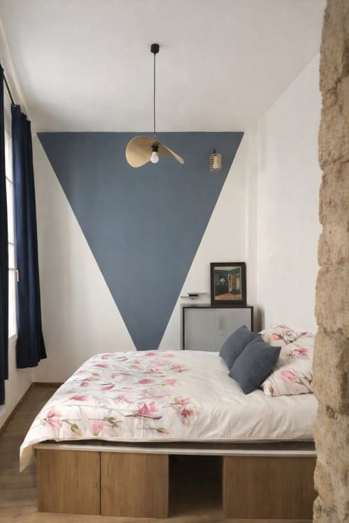 Chambre d'appartement parisien moderne avec accent mural géométrique bleu, literie florale, luminaire suspendu et cadre de lit en bois