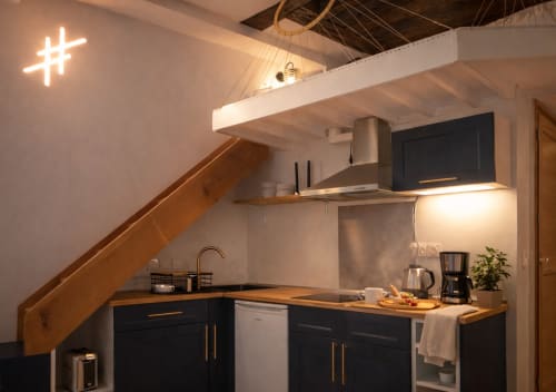 Petite cuisine moderne de l'appartement ATHEA Paris avec meubles noirs, plan de travail en bois et enseigne néon hashtag