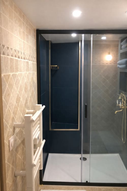 Élégante douche avec murs noirs et finitions dorées dans cet appartement ATHEA Paris, aux carrelages géométriques