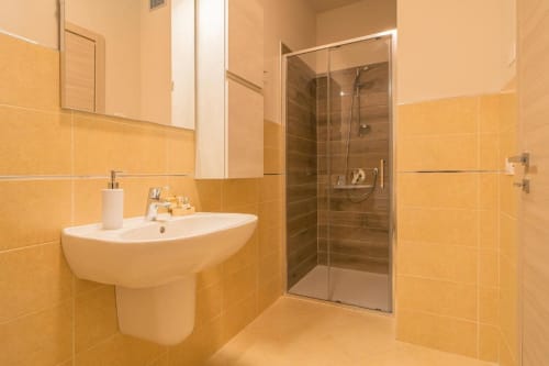 Bagno moderno presso Le Alpi bed & living a Cividale Camuno con piastrelle gialle, lavabo a colonna e cabina doccia.