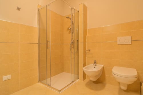 Bagno moderno a Le Alpi bed & living a Cividale Camuno con box doccia in vetro, bidet, WC e rivestimenti in piastrelle dorate