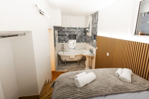 Chambre confortable d'appartement parisien avec salle de bain attenante, baignoire, literie rayée, parquet et vue sur la ville.