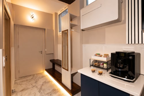 Kitchenette moderne dans un appartement parisien avec cafetière noire, plan de travail blanc et éclairage ambiant