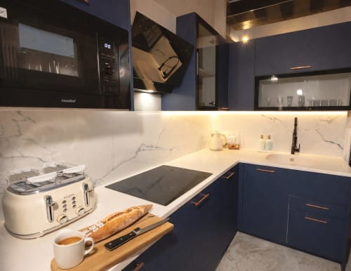 Cuisine moderne dans un appartement parisien avec armoires bleu marine, dosseret en marbre, plaque de cuisson par induction et comptoirs blancs