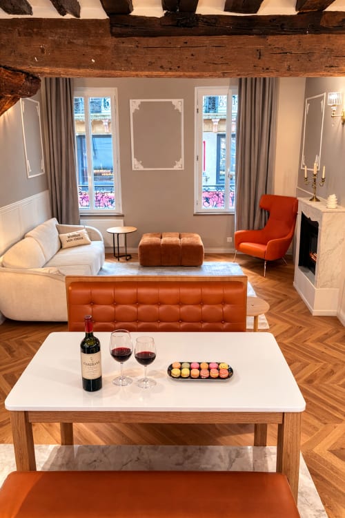 Élégant salon parisien avec canapé crème, accents orange, cheminée, vue sur la ville, vin et macarons sur table basse