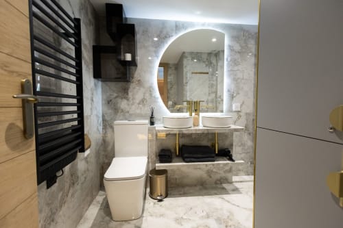 Salle de bain moderne dans un appartement parisien avec murs en marbre, deux vasques, miroir arqué rétroéclairé et sèche-serviettes noir chauffant